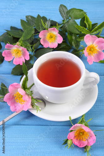 Cup of tea and wild rose flower on blue boards