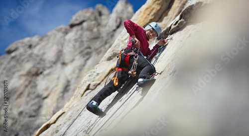 Fotografija Young woman climber selects tools while processing the route while on a safety station on a vertical rock wall in the mountains, close-up, panorama