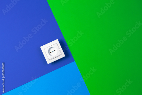 White electrical power socket on light blue, navy and green background. Top view, copy space for text