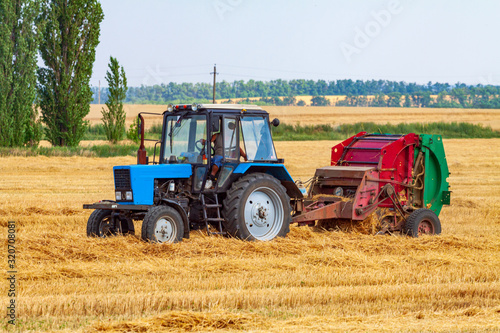 A tractor with a trailed bale making machine collects straw rolls in the field and makes round large bales