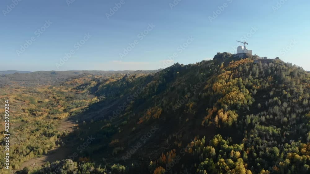 Astronomical Observatory on peak of high mountain in Scenic epic autumn landscape. Aerial drone view of construction crane at top of hill, yellow colored leaves on trees, scientific research activity Astronomical Observatory on peak of high mountain in Scenic epic autumn landscape. Aerial drone view of construction crane at top of hill, yellow colored leaves on trees, scientific research activity