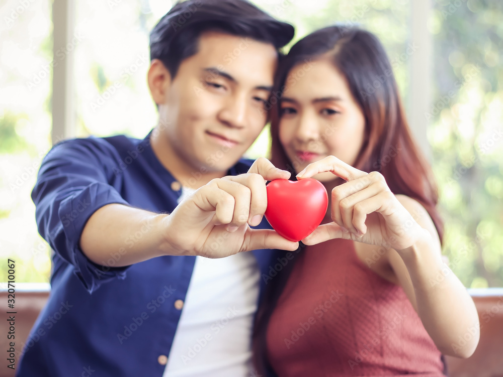 young Asian couple sitting close together holding red hearts in their hands. Selective focus on red heart. young Asian couple sitting close together holding red hearts in their hands. Selective focus on red heart.