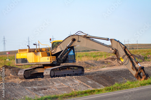 A large iron excavator bucket collects and pours sand rubble and stones in a quarry at the construction site of road facilities and houses