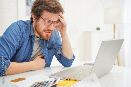 Foto Worried man sitting in home office and using credit card
