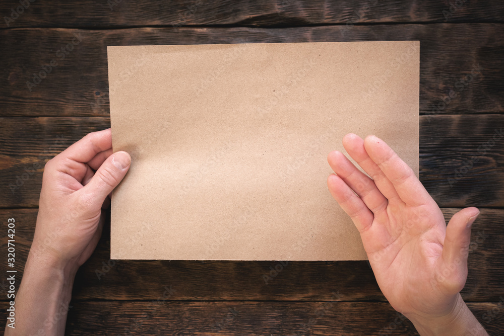 Blank brown paper page in male hands on wooden desk flat lay background. Blank brown paper page in male hands on wooden desk flat lay background.