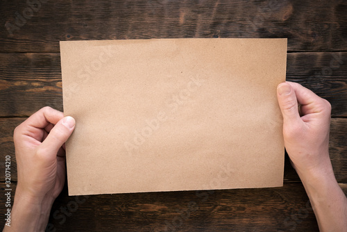 Blank brown paper page in male hands on wooden desk flat lay background. photo