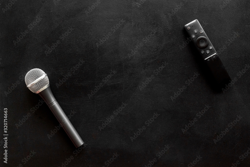Naklejka premium TV news concept. TV remote and microphone on black background top-down copy space