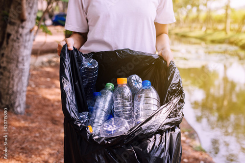 Woman volunteer holding black color garbage bag with plasatic bottle at park,Dispose recycle and waste management concept photo