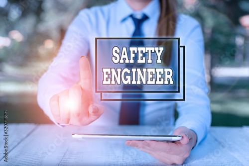 Conceptual hand writing showing Safety Engineer. Concept meaning demonstrating who inspects all possible danger spots in a factory Female business person sitting by table and holding mobile phone photo