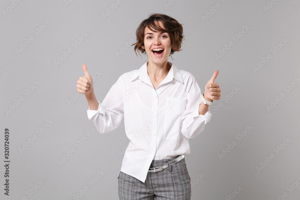 Cheerful funny young brunette business woman in white shirt posing isolated on grey wall background studio portrait. Achievement career wealth business concept. Mock up copy space. Showing thumbs up. Cheerful funny young brunette business woman in white shirt posing isolated on grey wall background studio portrait. Achievement career wealth business concept. Mock up copy space. Showing thumbs up.