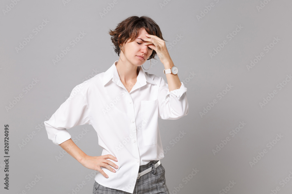 Tired young business woman in white shirt posing isolated on grey background studio portrait. Achievement career wealth business concept. Mock up copy space. Keeping eyes closed, put hand on nose. Tired young business woman in white shirt posing isolated on grey background studio portrait. Achievement career wealth business concept. Mock up copy space. Keeping eyes closed, put hand on nose.