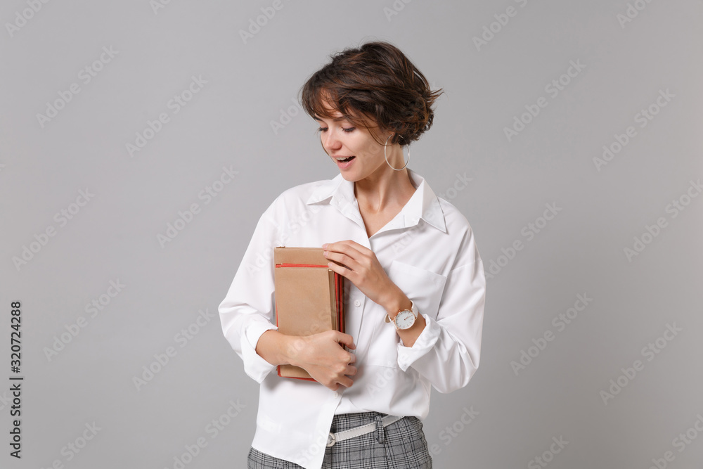 Attractive young business woman in white shirt posing isolated on grey wall background studio portrait. Achievement career wealth business concept. Mock up copy space. Holding books, notebooks. Attractive young business woman in white shirt posing isolated on grey wall background studio portrait. Achievement career wealth business concept. Mock up copy space. Holding books, notebooks.