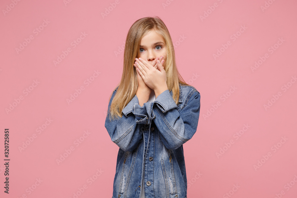 Shocked little blonde kid girl 12-13 years old in denim jacket isolated on pastel pink background children studio portrait. Childhood lifestyle concept. Mock up copy space. Covering mouth with hands. Shocked little blonde kid girl 12-13 years old in denim jacket isolated on pastel pink background children studio portrait. Childhood lifestyle concept. Mock up copy space. Covering mouth with hands.