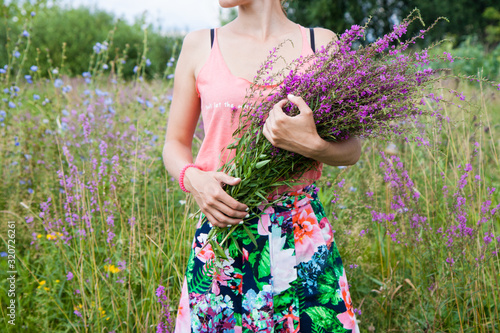 Young woman in the field holding a bunch with wild lilac, purple and vilet flowers. 