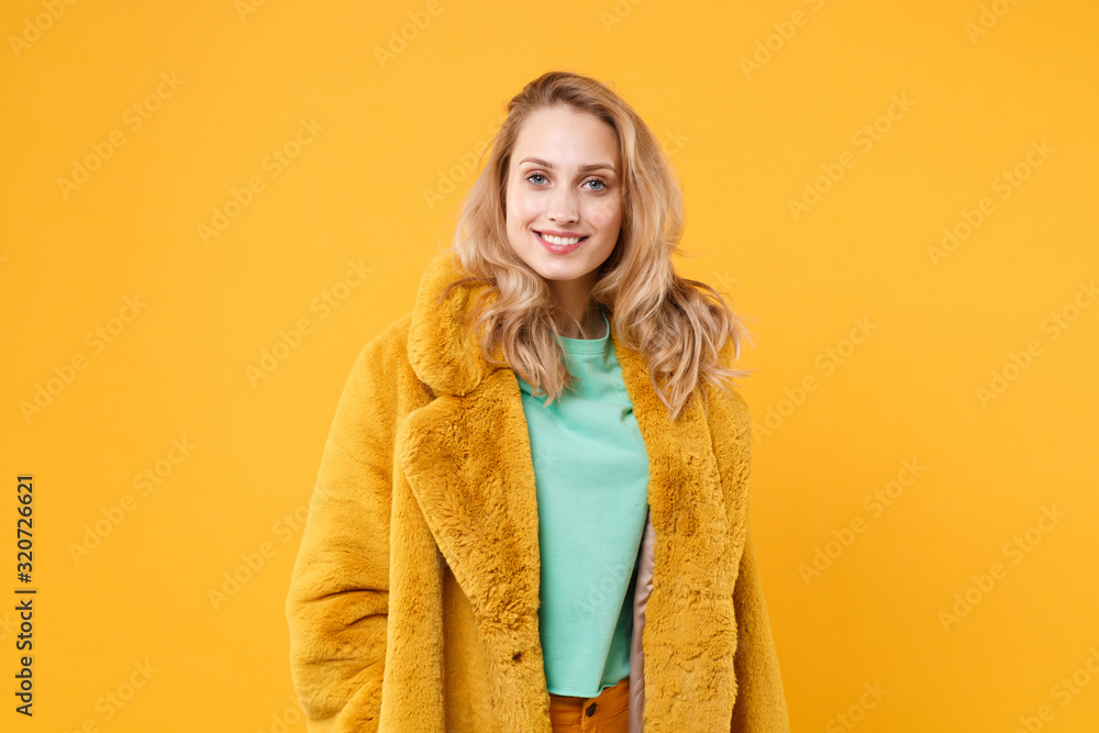 Smiling beautiful young blonde woman girl in yellow fur coat posing isolated on orange wall background studio portrait. People sincere emotions lifestyle concept. Mock up copy space. Looking camera. Smiling beautiful young blonde woman girl in yellow fur coat posing isolated on orange wall background studio portrait. People sincere emotions lifestyle concept. Mock up copy space. Looking camera.