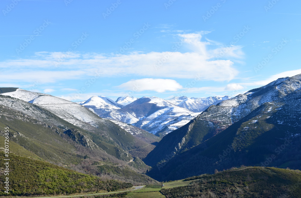 Winter landscape with snowy mountains and green valley with forest on a sunny day. Ancares, Lugo, Galicia, Spain.