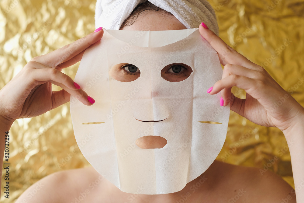 Φωτογραφία Young woman apply cosmetic fabric facial mask on golden background