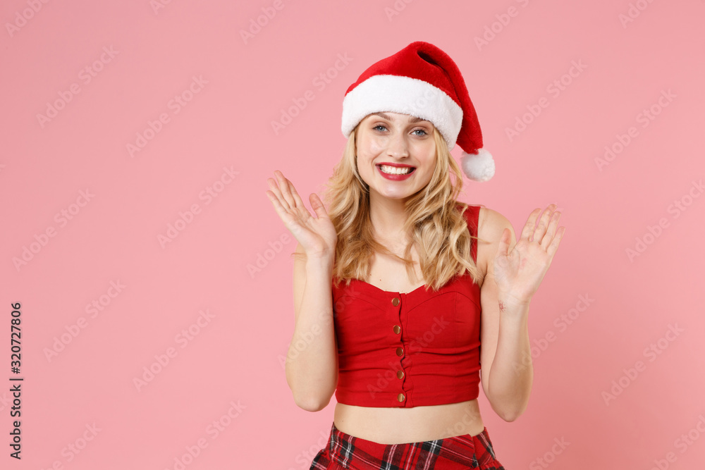 Smiling young blonde woman girl in red sexy clothes, Christmas hat isolated on pastel pink background in studio. Happy New Year 2020 celebration holiday concept. Mock up copy space. Spreading hands.