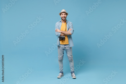 Laughing traveler tourist man in yellow casual clothes with photo camera isolated on blue background. Male passenger traveling abroad on weekends. Air flight journey concept. Holding hands crossed.