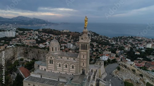Drone turning around the La Bonne Mere statue at the top of Marseille, South of France,in early morning with a very nice sunrise sunlight and dark sky and sea in background