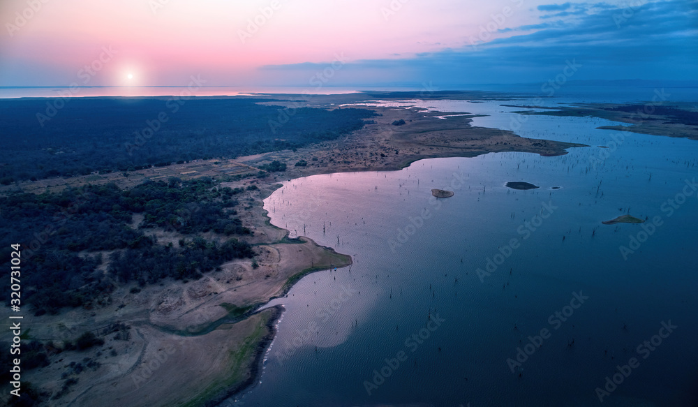 Aerial view of african lake Kariba and surrounding landscape in late evening with setting sun. Blue and pink colors. Dead trees in the water. Zimbabwe. Safari camping on the shore of lake Kariba.