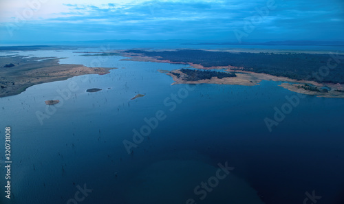 Aerial view of african lake Kariba and surrounding landscape in late evening with setting sun. Blue and pink colors. Dead trees in the water. Zimbabwe. Safari camping on the shore of lake Kariba.