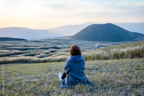 Lovely cute japanese girl sitting on Aso active volcano background with smoke at Mount Aso Nakadake, Kumamoto, kyushu, Japan (photo grain some noise for film colour) photo