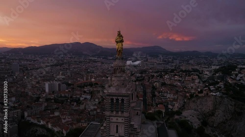 Drone moving forward to La Bonne Mere statue at the top of Marseille, South of France, with a very nice sunrise sunlight and dark sky.