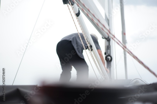 Back of an older man working at the main mast on a sailing boat