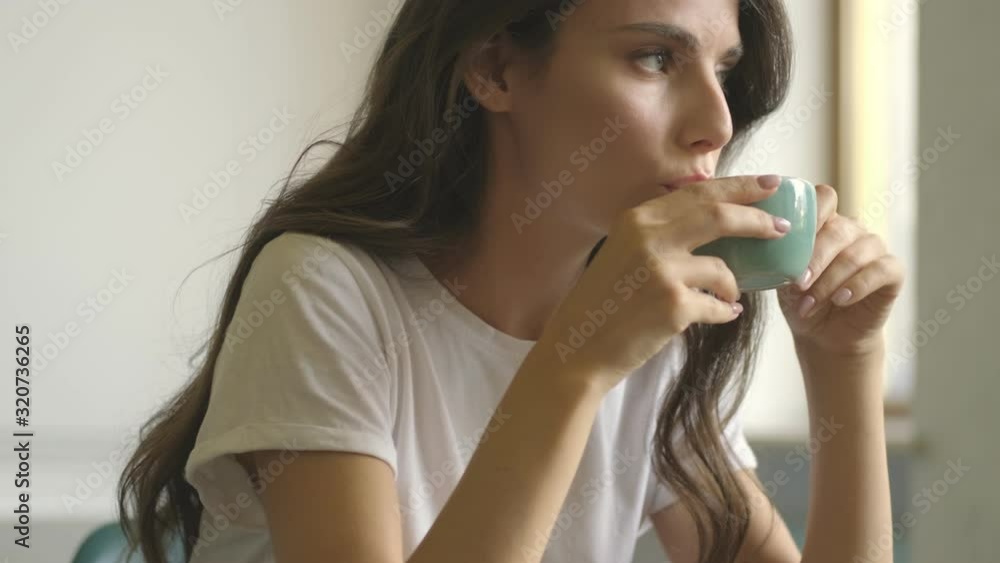 Concentrated serious young woman is drinking coffee while working with a laptop indoors Concentrated serious young woman is drinking coffee while working with a laptop indoors