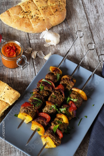 drei spieße Schisch Kebab mit Lammfleisch Paprika und Zwiebeln auf grauem teller und Holztisch Pitabrot ajvar und knoblauch im Hintergrund  photo