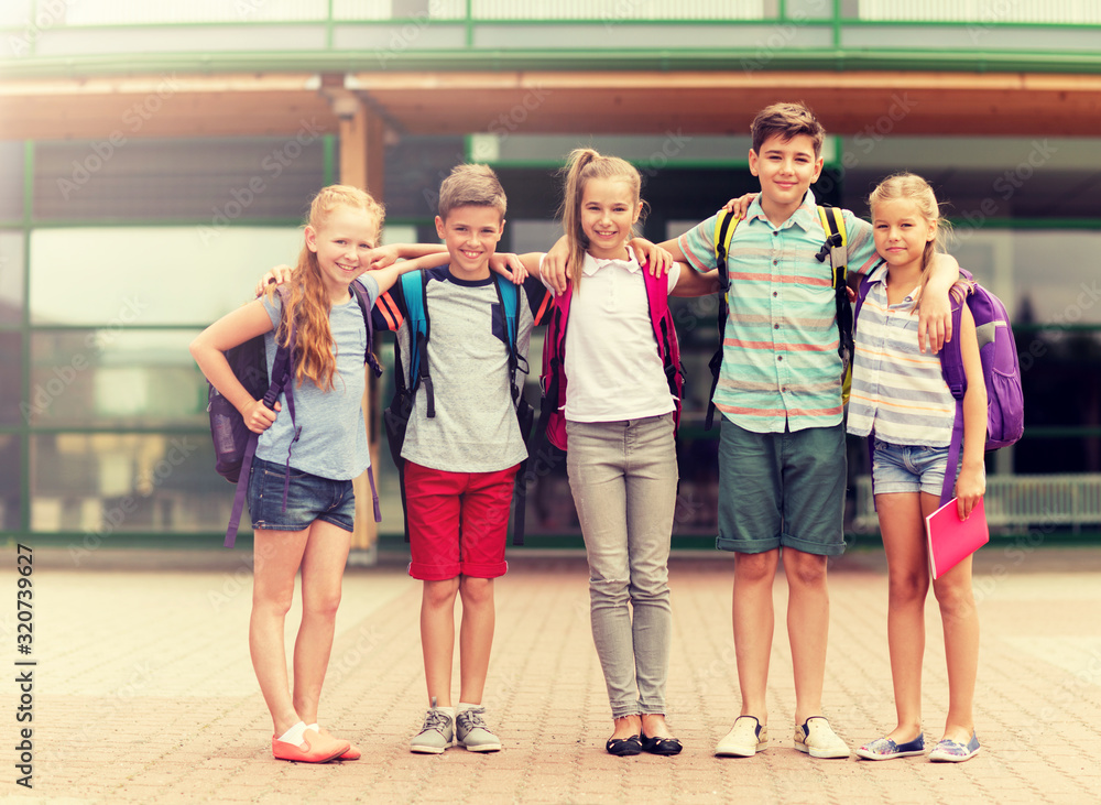 Fototapeta premium primary education, friendship, childhood and people concept - group of happy elementary school students with backpacks hugging outdoors