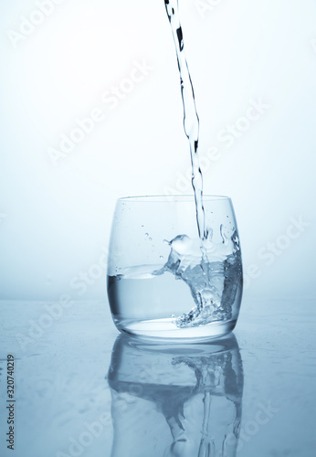 A stream of water flowing into a transparent glass cup with a splash of drops and drops. A jet of clean drinking spring water pouring into a glass