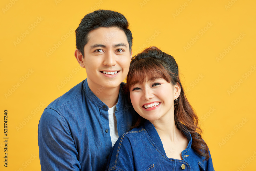 Happy casual couple embracing, posing to camera on yellow studio background Happy casual couple embracing, posing to camera on yellow studio background