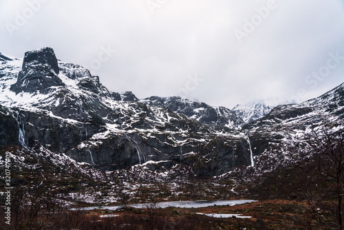 Winter mountain landscape with small waterfall flows into a lake. Lofoten islands, Norway.
