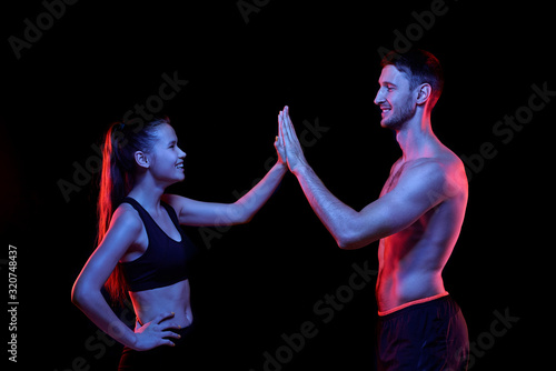 Young successful sportsman and sportswoman giving each other high five and laughing against black background photo