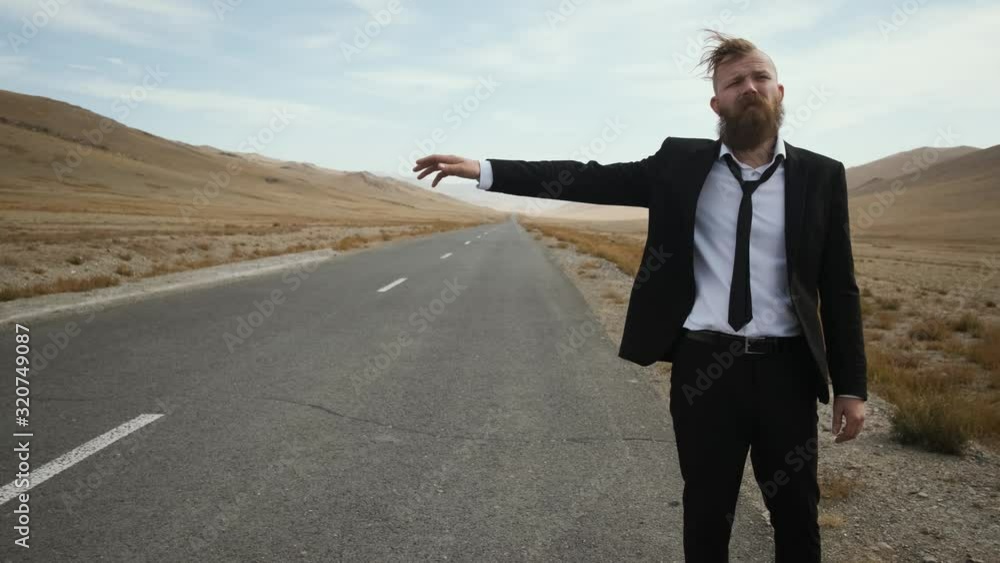 man with beard mustache black suit with tie in sneakers with white soles office worker stands on the road steppe, catches car, close-up, pensive, looks into the distance caucasian man with beard mustache black suit with tie in sneakers with white soles office worker stands on the road steppe, catches car, close-up, pensive, looks into the distance caucasian
