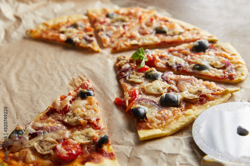 close up view of cut delicious italian pizza with olives on baking paper with pizza knife on wooden table close up view of cut delicious italian pizza with olives on baking paper with pizza knife on wooden table