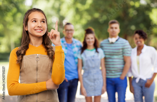 friendship, idea and people concept - happy smiling young teenage girl pointing finger up over group of friends at park on background