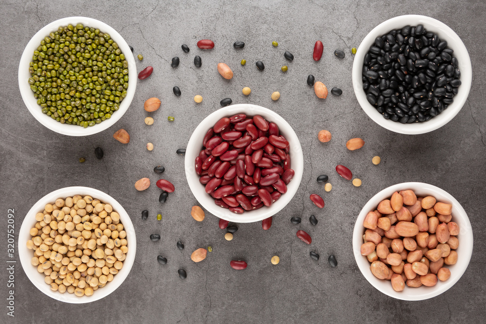 Grains or beans, red bean, black bean, green bean, soybean, peanut in the white bowl placed on the black cement floor. Top view. Grains or beans, red bean, black bean, green bean, soybean, peanut in the white bowl placed on the black cement floor. Top view.