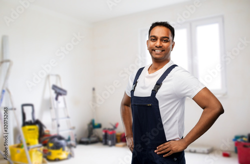 profession, construction and building - happy smiling indian worker or builder over room with working equipment at new home or apartment background