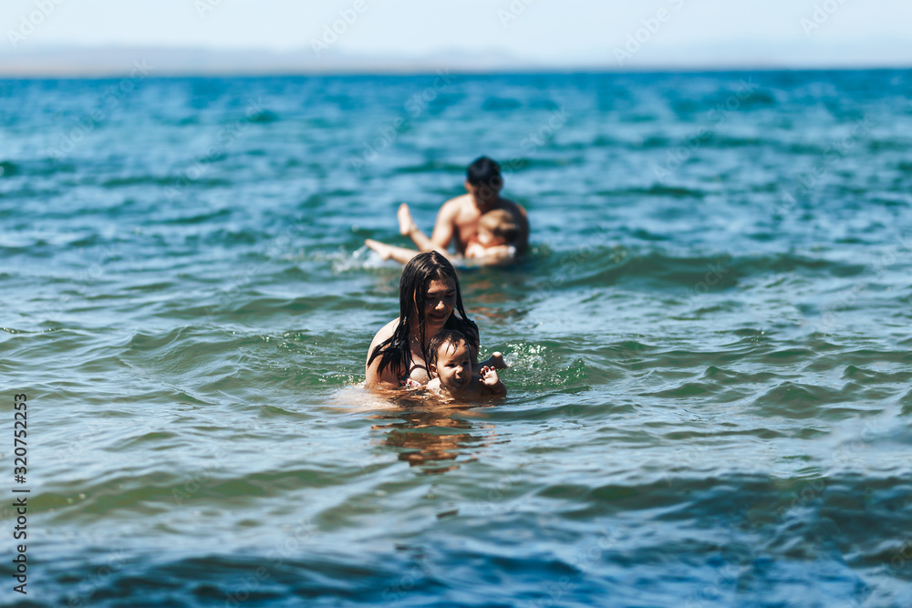 Young family, mother father and babies, jumping in the blue sea, Hello summer