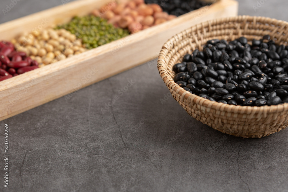 Black beans and grains in the wooden basket and in the wooden tray placed on the black cement floor. High angle view. Black beans and grains in the wooden basket and in the wooden tray placed on the black cement floor. High angle view.