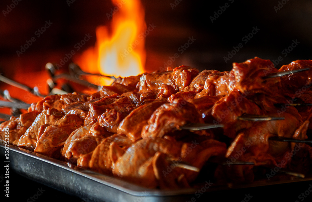 Close up of some meat skewers grilled in a barbecue. Barbecue grill, seasoned meat strung on skewers against the backdrop of the fire of a blazing fireplace in an expensive natural food restaurant Close up of some meat skewers grilled in a barbecue. Barbecue grill, seasoned meat strung on skewers against the backdrop of the fire of a blazing fireplace in an expensive natural food restaurant