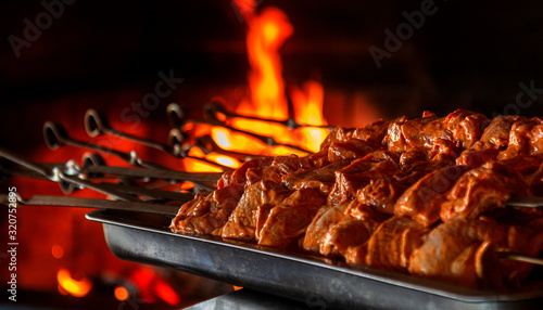 Close up of some meat skewers grilled in a barbecue. Barbecue grill, seasoned meat strung on skewers against the backdrop of the fire of a blazing fireplace in an expensive natural food restaurant