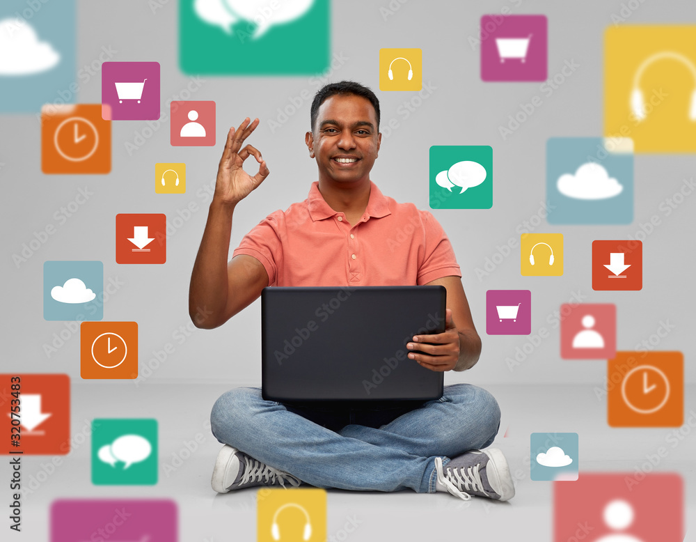 technology and people concept - happy indian man with laptop computer sitting on floor and showing ok hand sign over mobile app icons on grey background technology and people concept - happy indian man with laptop computer sitting on floor and showing ok hand sign over mobile app icons on grey background