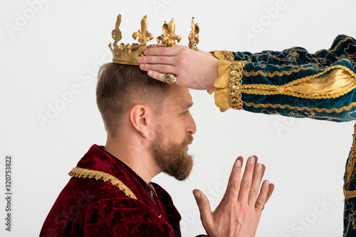 Obraz na plátně cropped view of man putting crown on king with praying hands on grey background