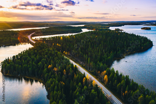 Aerial view of road in green summer forest with blue lakes at sunset in Finland