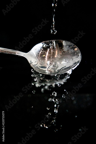 Studmień wody odbijający się o łyżkę, czarne tło, krople wody © andsko