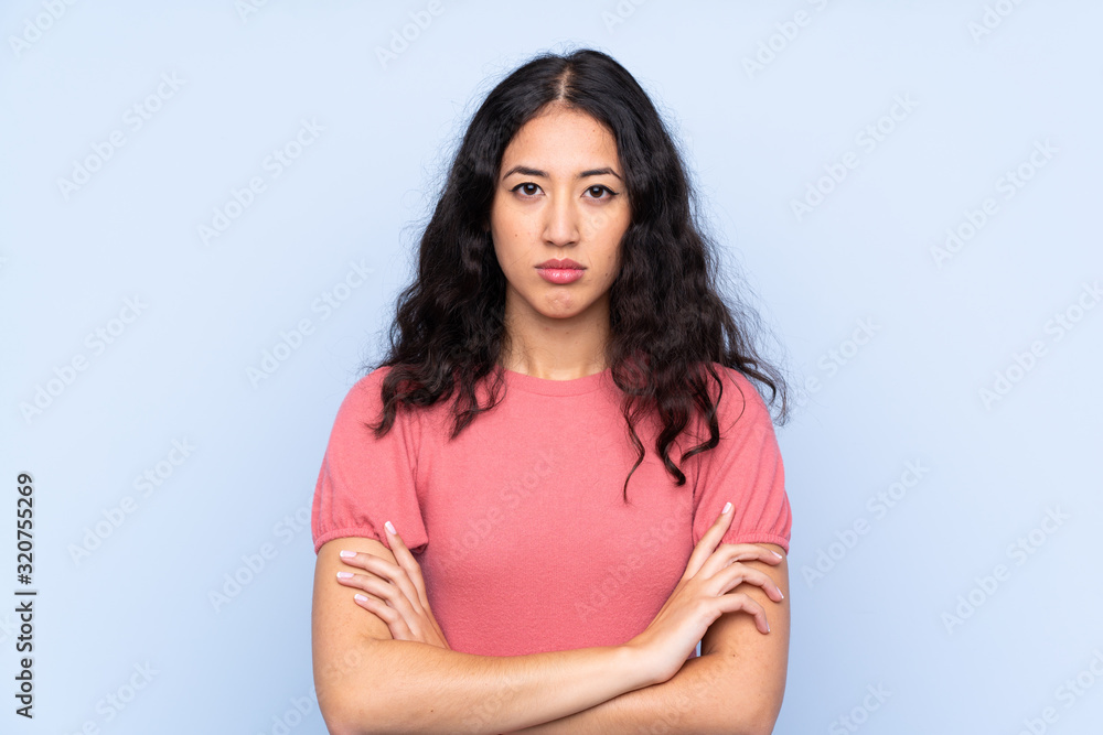 Mixed race woman wearing a sweater over isolated blue background keeping arms crossed Mixed race woman wearing a sweater over isolated blue background keeping arms crossed